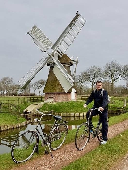 Chris Heckmann posing in front of a windmill in the Netherlands with his bike
